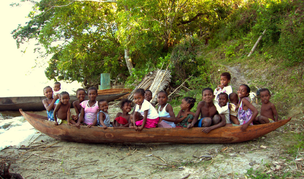 Some kids sitting in a canoe in a rural village.